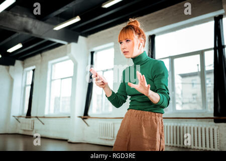 Rothaarige professionelle Yogalehrer in einer grünen Rollkragen Holding ein Telefon in der Hand. Stockfoto