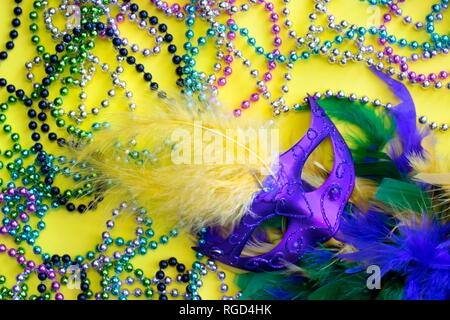Eine Auswahl an bunten Dekorationen für die Mardi Gras Festival auf einem gelben Hintergrund, einschließlich Venezianische Maske, gefiederten Boa und Mardi Gras Perlen. Stockfoto