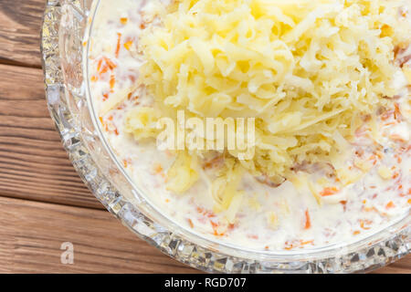 Wie man Mimosa, einen russischen Fischsalat, zubereitet. Kristallschale mit einer Schicht geriebener Kartoffeln Stockfoto