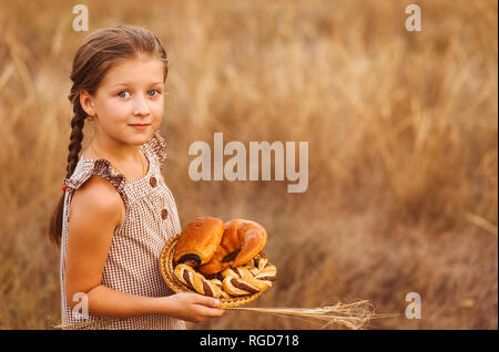 Mädchen mit Brot und Brötchen im Korb. Kind hält eine Menge Brote in den Händen in das Feld ein. Stockfoto