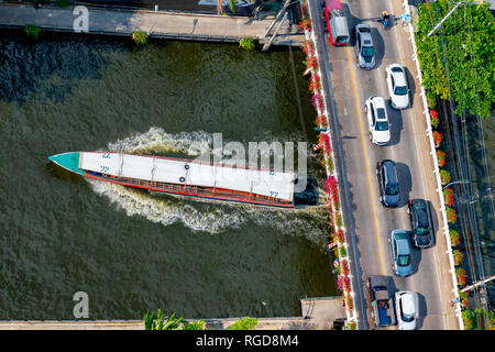 Luftbild des Autos auf einer Brücke über einen Kanal in Bangkok und Pendler Boot unter vorbei. Stockfoto