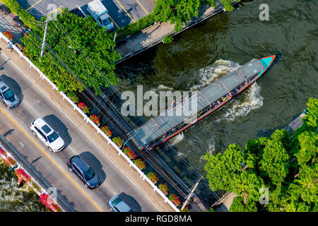 Luftbild des Autos auf einer Brücke über einen Kanal in Bangkok und Pendler Boot unter vorbei. Stockfoto