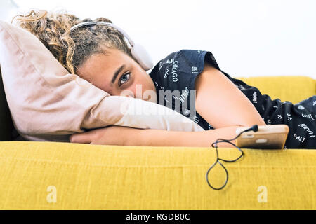 Mädchen auf der Couch liegen zu Hause Musik hören mit Kopfhörern und Smartphone Stockfoto