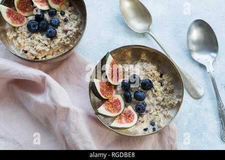 Schalen mit Porridge mit in Scheiben geschnittenen Feigen, Blaubeeren und getrockneten Beeren Stockfoto