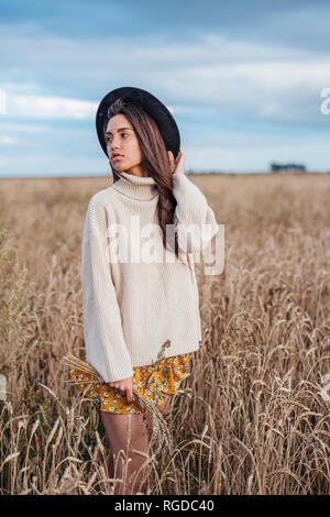 Porträt der jungen Frau mit Hut und oversized rollkragen pullover in Maisfeld Stockfoto