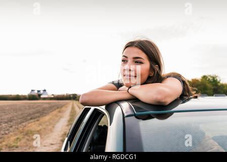 Lächelnde junge Frau aus schiebedach eines Autos Stockfoto