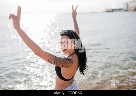 Portrait von funkelnden junge Frau, die an der Küste übersicht Sieg Zeichen Stockfoto