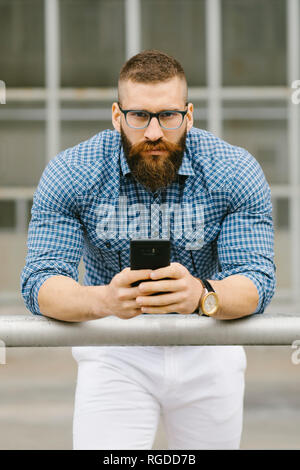 Portrait von bärtigen hipster Geschäftsmann mit Smartphone schiefen Zusatzscheinwerfer auf dem Dach Stockfoto