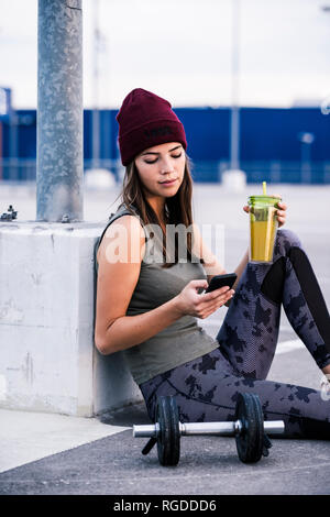 Junge Frau sitzt auf dem Boden nach kurzhanteltraining, mit Smartphone Stockfoto