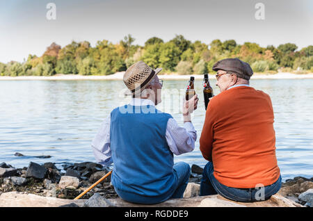 Alte Freunde sitzen am Flussufer, Bier trinken. Stockfoto