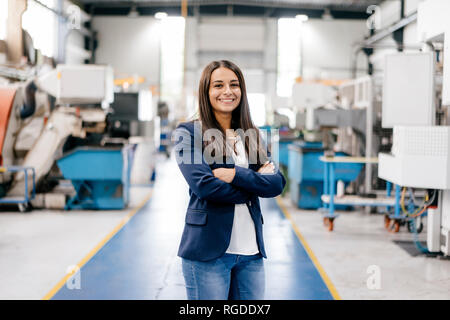 Selbstbewusste Frau, die in High-Tech-Unternehmen, die in der Fabrik Workshop mit gekreuzten Armen Stockfoto