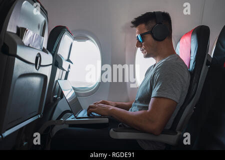 Mann im Flugzeug, mit Laptop, Kopfhörer Stockfoto