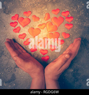 Das Symbol der Liebe und der Gesundheit ist das Herz in männlichen Händen. Das brennende Herz ist aus kleinen Herzen in den männlichen Palmen gelegt. Stockfoto