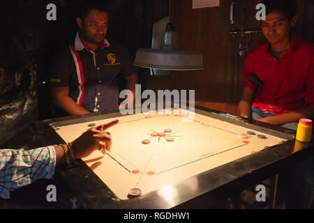 Drei Männer in einem schmuddeligen, dunklen Hinterhof "Club" in Mumbai, Indien, spielen der beliebten tabletop Carrom (CAROM) Stockfoto