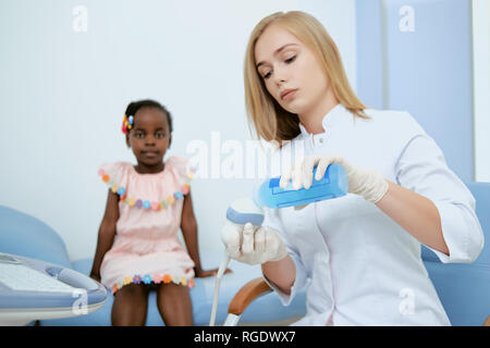 Erntegut Detailansicht von Arzt und kleines Mädchen in rosa Kleid saßen und von der Kamera. Junge Frau sitzt und prepairing Für medizinische Beratung im Krankenhaus. Konzept der Gesundheitsversorgung. Stockfoto