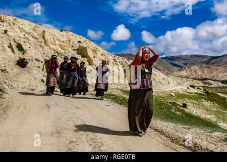 Eine Gruppe von einheimischen Frauen, die Körbe, entlang einer Schotterstraße in die karge Landschaft des Oberen Mustang Stockfoto