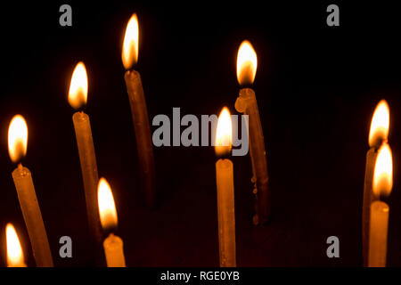 Viele Weihnachten Kerzen brennen in der Nacht auf dem schwarzen Hintergrund. Kerze Flamme in schwarzen Hintergrund isoliert. Gruppe von brennenden Kerzen in der Dunkelheit mit Stockfoto