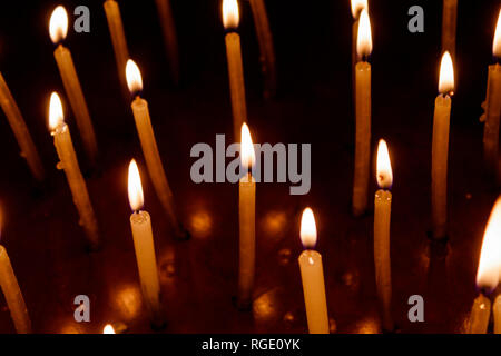 Viele Weihnachten Kerzen brennen in der Nacht auf dem schwarzen Hintergrund. Kerze Flamme in schwarzen Hintergrund isoliert. Gruppe von brennenden Kerzen in der Dunkelheit mit Stockfoto