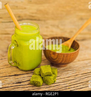 Grüner Tee Latte mit Eis im Marmeladenglas, Matcha Pulver und Süßigkeiten aus Matcha auf Holz- Hintergrund. Hausgemachte Eistee Matcha Latte Tee mit Milch Null Stockfoto