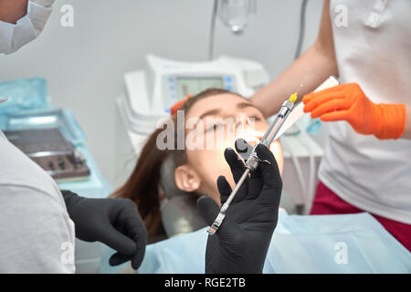 Zahnarzt in Schutzhandschuhe, schoß in den Händen und Tun betäubend auf Client vor. Weibliche Patienten auf dem Behandlungsstuhl im Hintergrund liegt. Konzept der Zähne Pflege und Behandlung. Stockfoto