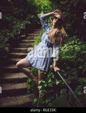 Schöne junge Mädchen in einem blauen Kleid auf Treppen im Freien mit Sonnenbrille, kurzes Kleid posiert, Beine zeigen auf der Treppe im Freien Sonnenbrillen tragen, sh Stockfoto