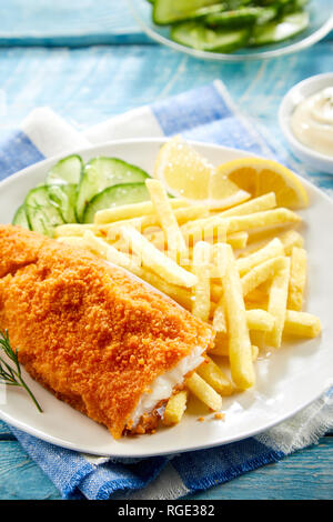 Knusprig frittierte Filet vom Kabeljau mit Brotkrumen mit Pommes Frites und frischem Gurkensalat serviert. Stockfoto