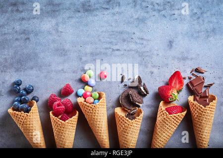 Zutaten für Spezialität Eis Verschütten von Kegel auf eine Grau texturierte Schiefer Hintergrund mit Oreos, Erdbeeren, Himbeeren, Heidelbeeren, sug Stockfoto