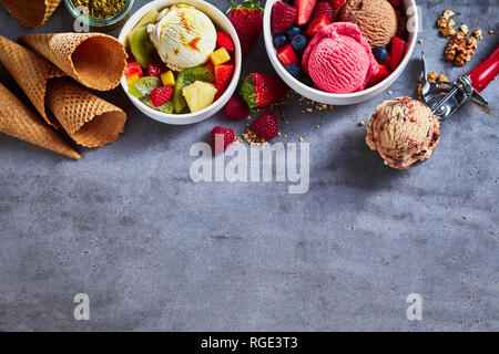 Sommer Eis Aromen mit frischem Obstsalat, verschiedene Beeren, Nüsse, Zucker, Kegel und eine Kugel als Grenze auf strukturierte Schiefer mit Platz kopieren Stockfoto