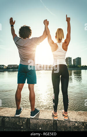 Eine schöne, junge Paar steht auf einer Wand neben dem Fluss und Gruß an die Sonne nach dem Training. Stockfoto