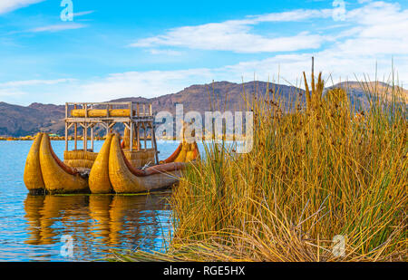 Ein totora Reed Boot durch die schwimmenden Inseln der Uros bei Sonnenaufgang mit der Anden im Hintergrund in der Nähe von Puno, Peru, Südamerika. Stockfoto