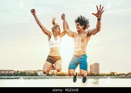 Schöne junge Paar lächelt und Springen nach erfolgreicher Ausbildung durch den Fluss in den Sonnenuntergang. Stockfoto