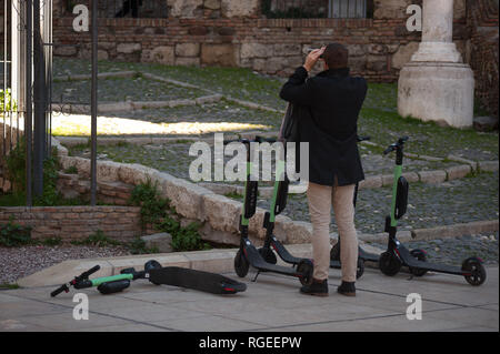 Kostenlose Scooter sind zu sehen auf der Straße geparkt als Tourist nimmt Fotos ein Denkmal. Der spanische General Traffic Management wird von nun an einen Führerschein für die elektroroller und eine Versicherung unter anderem Maßnahmen bedarf, entsprechend einer neuen Dekret von der spanischen Regierung. In den letzten Monaten hat mehr Unfälle mit Elektroroller passiert, und ein Tod im vergangenen Jahr. Die Regierung erwarten, wie dies der Verwendung dieser Transporte zu regulieren und die Sicherheit verbessern. Stockfoto