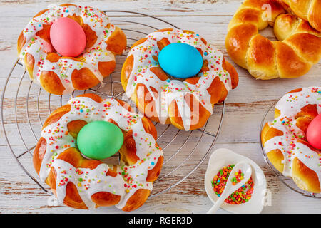 Hausgemachtes Italienisches Osterbrot Ringe mit gefärbten Eiern auf einem alten weißen Holz- Tabelle, Ansicht von oben, close-up Stockfoto