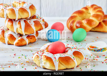 Nahaufnahme der einzelnen süßen italienischen geflochtenes Ostern Brot Ringe verglast, um gefärbtes Ei und gekrönt mit bunten Streuseln am Draht Rack, auf einer alten wh Stockfoto