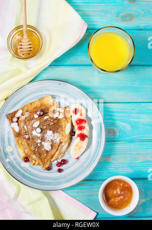 Traditionelle Pfannkuchen mit Banane und Beeren auf Blau Holz- Hintergrund. Ansicht von oben Stockfoto