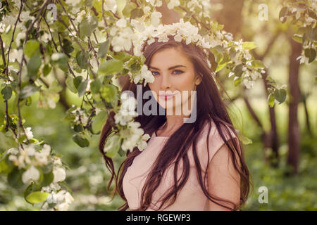 Junge Frau mit Blumen im Freien. Schöne Brünette fashion model Mädchen mit langem Haar und Make-up auf grünen Blättern und weißen Blüten ba Stockfoto