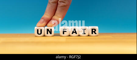 Würfel Form das Wort "unfair" während zwei Finger die Buchstaben "UN" drücken, um das Wort "FAIR" zu ändern. Stockfoto