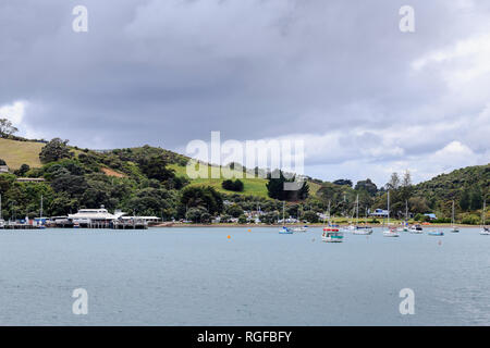 Annäherung an Matiatia Wharf im Hafen von Waiheke Island. Segelboote (Yachten) in der Bucht vor Anker, sanfte Hügel hinter sich. Stockfoto