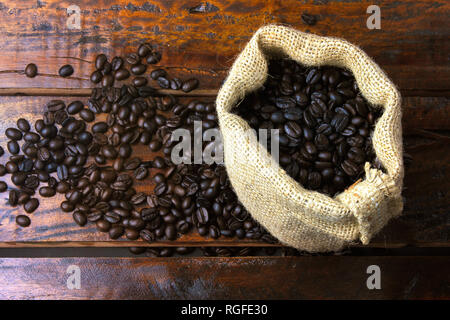 Geröstet und frisch gemahlenen Bohnen in rustikalen Stofftasche und in rustikalen Holztisch gegossen. Ansicht von oben Stockfoto