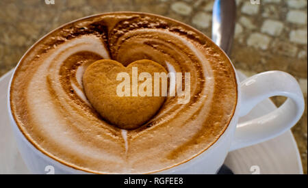 Cappuccino mit einem Herzförmigen Biskuit in der Mitte der Schaum Stockfoto