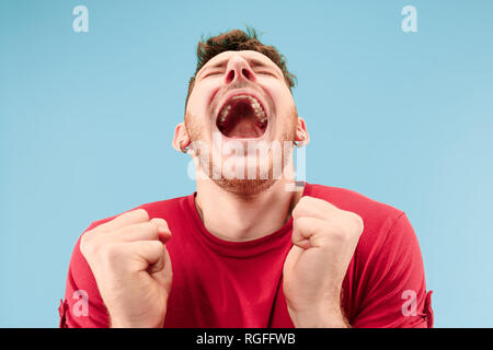 Ich gewann. Gewinnen Erfolg glücklich feiern Sein ein Sieger. Dynamisches Bild der kaukasischen männliches Modell auf Blau studio Hintergrund. Sieg, Freude Konzept. Menschlichen gesichts Emotionen Konzept. Trendige Farben Stockfoto