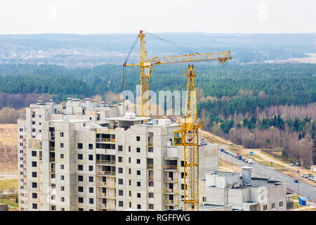 Panoramablick auf Turmdrehkrane und unvollendete multi-stöckiges Hochhaus in der Nähe von Gebäuden unter Baustelle in der sonnigen Tag aus der Vogelperspektive mit fo Stockfoto