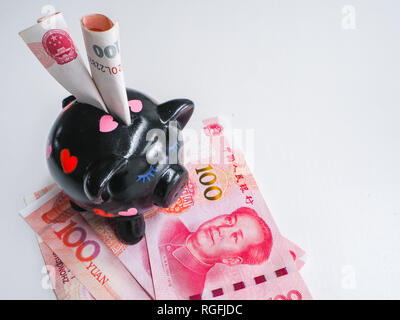 Schwarz Sparschwein neben Chinesisch 100 rmb Banknoten auf einem weißen Holz- Hintergrund. Das Schwein Symbole Vermögen im chinesischen Tierkreis. Stockfoto