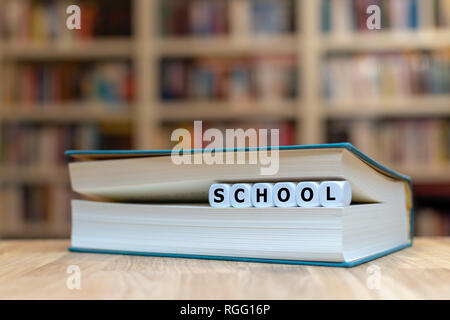 Würfel in Buchform das Wort 'Schule'. Das Buch liegt auf einem hölzernen Schreibtisch in einer Bibliothek. Stockfoto