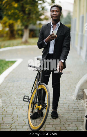 Portrait von gutaussehenden jungen Mann mit Handy und festen Gang Fahrrad auf der Straße. Stockfoto