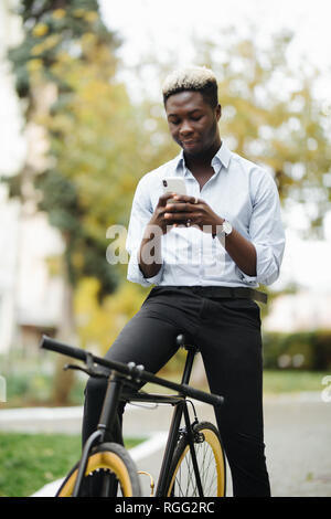 Afro junger Mann mit Handy und festen Gang Fahrrad auf der Straße. Stockfoto