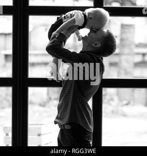 Junger Vater spielt mit seinem kleinen Sohn und wirft seine gegen Fenster Hintergrund. Schwarz-weiß-Bild. Stockfoto