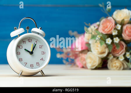Weiß Wecker und Blumen rosa und rote Rose auf Holztisch und blauer Hintergrund mit Kopie Platz für Text und Inhalt hinzufügen. Stockfoto