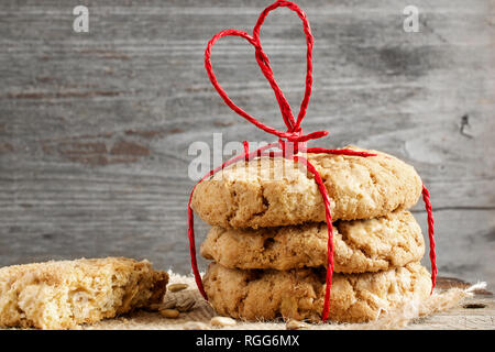 Stapel von oat Cookies für den Valentinstag mit roten herzförmigen Band auf Holztisch. Valentines Tag Hintergrund. Nach oben Schließen Stockfoto