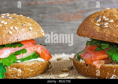 Zwei lachs Burger mit Gemüse auf rustikalen Holzmöbeln Hintergrund. gesundes Frühstück. Nach oben Schließen Stockfoto